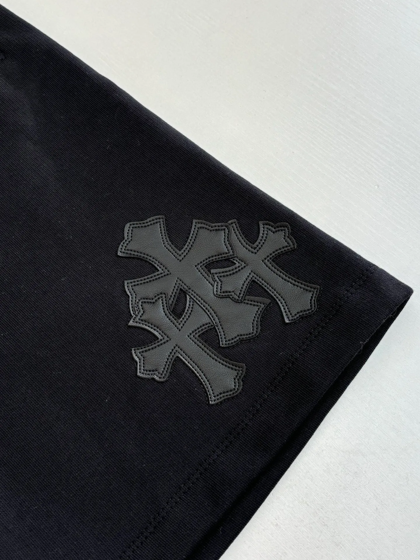 P346 Chrome Hearts*/Chrome Hearts 26SS early spring new patch embroidered shorts The fabric is made of a blended ratio of 80% cotton and 20% polyester. It is woven with a siro spinning process of 32-count base yarn and 10-count veil to form a high-weight terry cloth base of 380g/㎡. The cotton-polyester blended material combines the skin-friendly breathability of cotton and the anti-wrinkle shape retention of polyester. The high-weight fabric gives the trousers excellent stiffness and drape. The core technology is patch embroidery, which is completed with the help of TAJIMA computer embroidery machine. The black special-shaped patch is precisely sewn to the trouser fabric through lock stitches. The embroidery stitch density is even and the edges are neatly hemmed, forming a three-dimensional relief-like visual effect. Size: S/M/L/XL